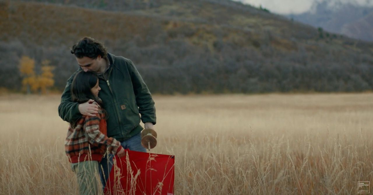 A father hugs his daughter in a field after flying a kite, and teaching her a lesson about the gospel of Jesus Christ