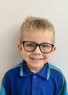 Portrait of a young boy in a blue shirt wearing glasses.