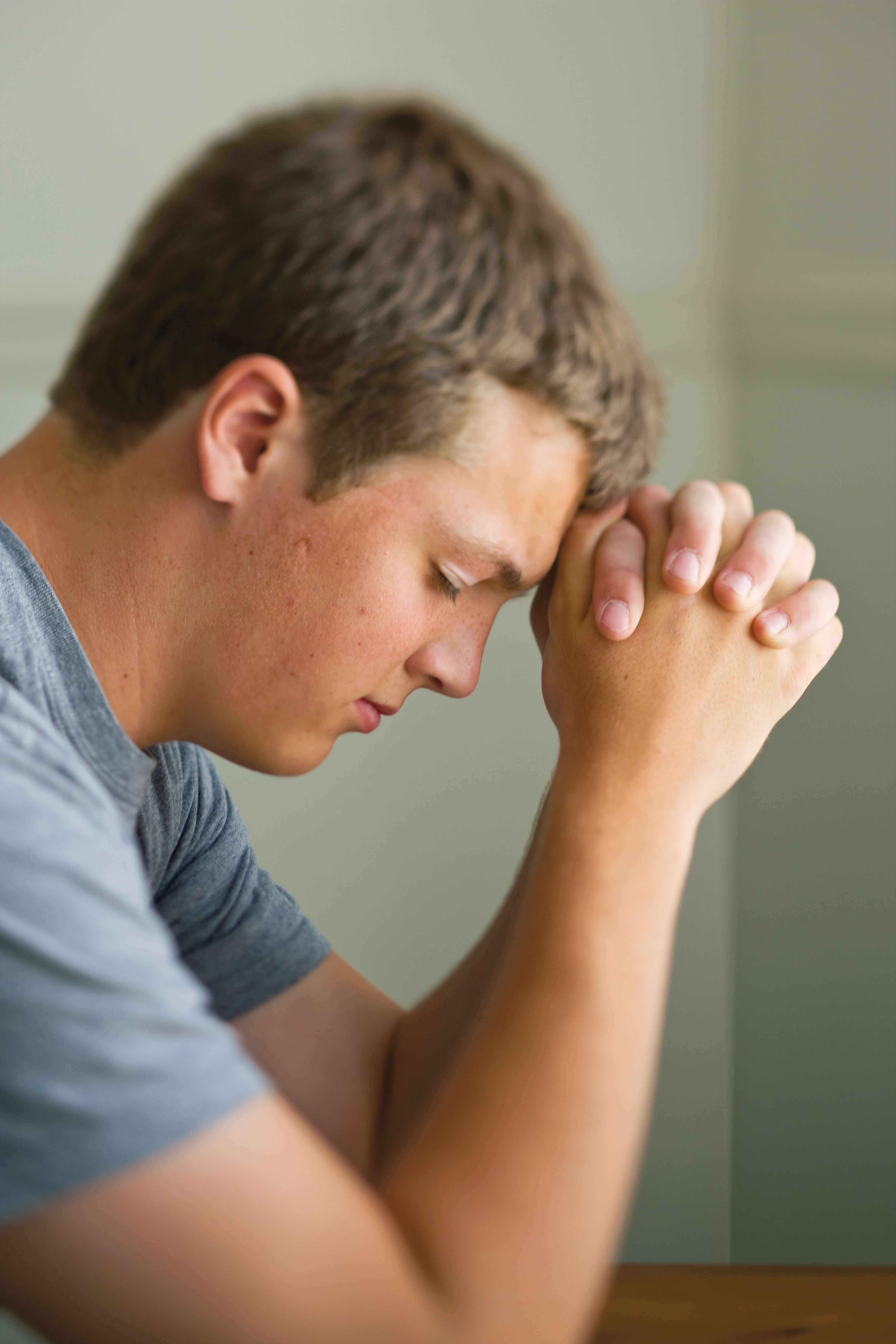 A young man bows his head and prays.