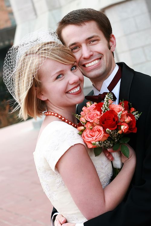 A portrait of a bride and groom embracing and smiling on their wedding day, while the bride holds a bouquet of flowers.