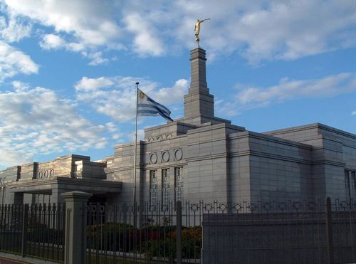 A side view of the entrance to the Montevideo Uruguay Temple, with the Uruguayan flag, in the evening.