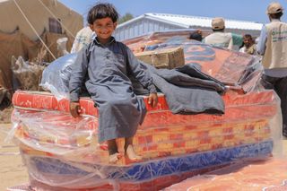 Child sitting on stack of mattresses, Yemen