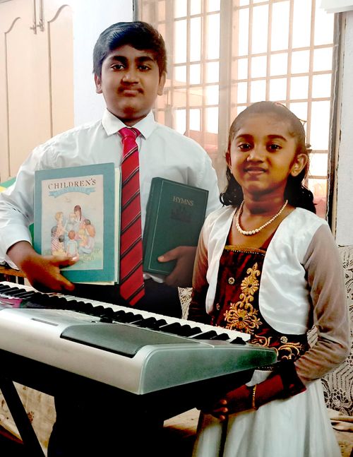 A boy and girl holding hymnbooks in front of a keyboard