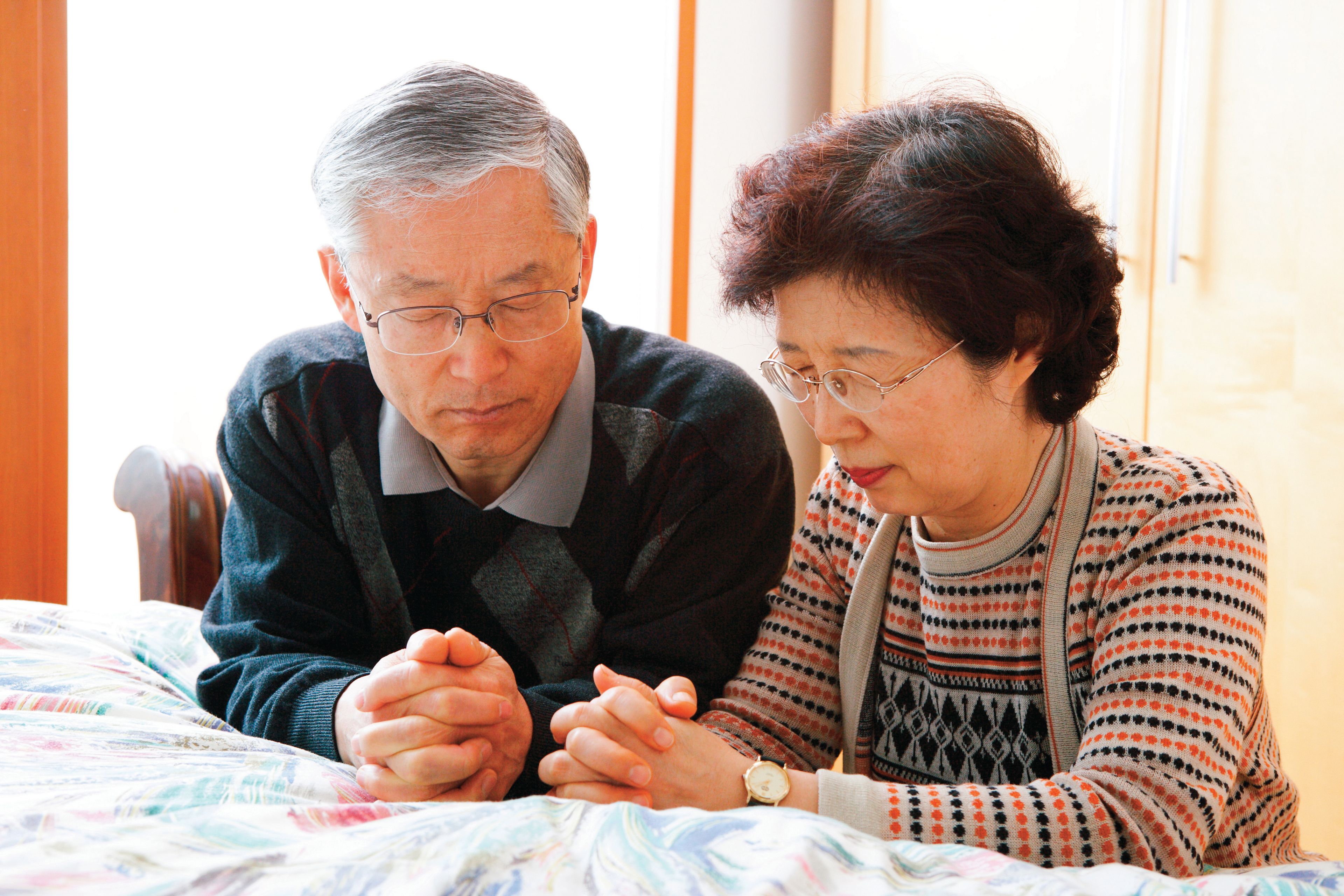 A couple kneeling by their bed to pray together.