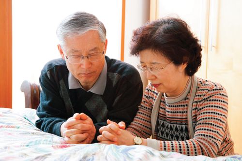 An elderly couple kneeling by their bed to pray together.