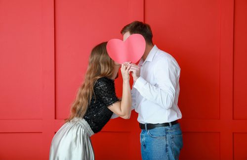 Young couple kissing behind a paper heart
