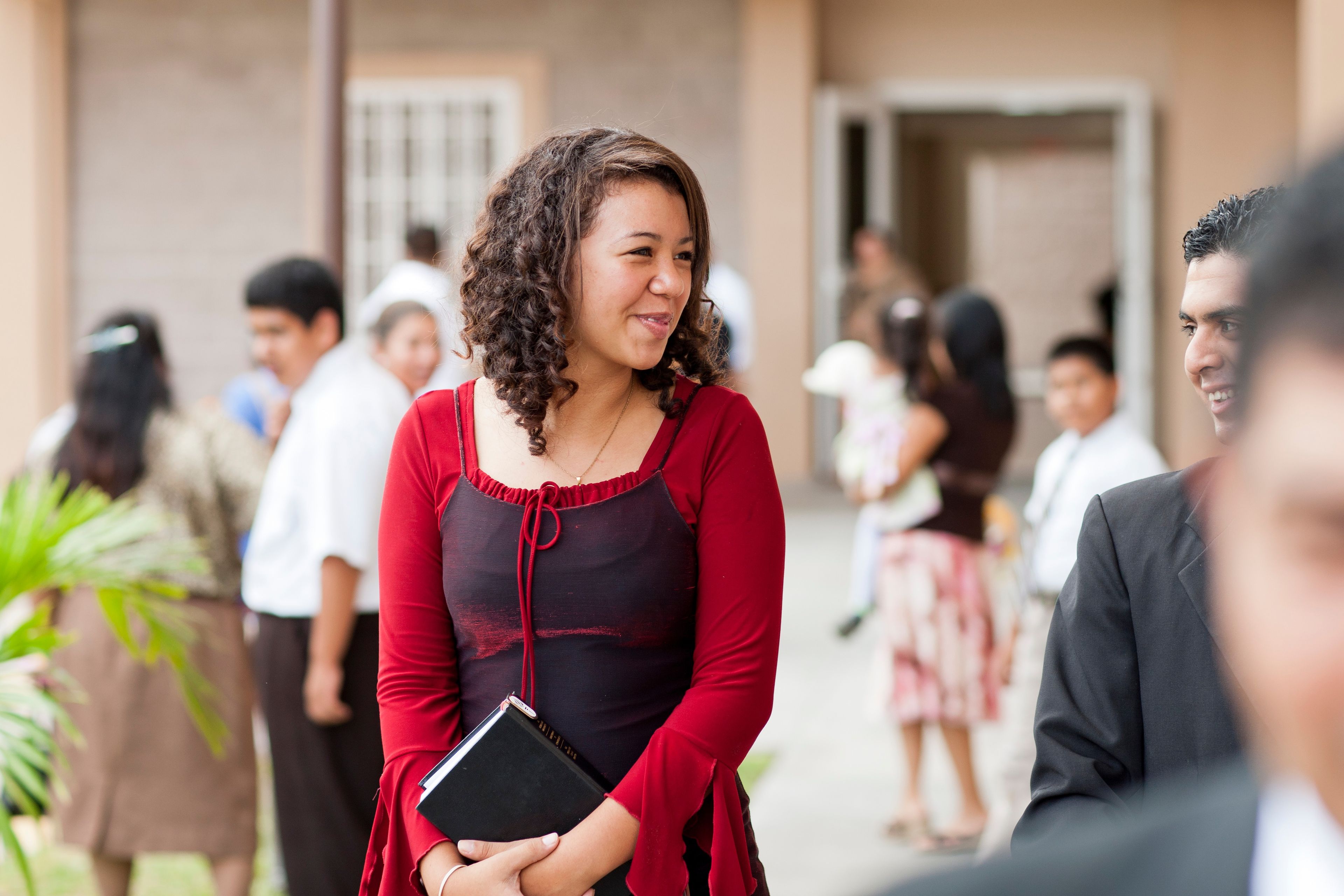 A portrait of a young woman holding scriptures outside a Church building in El Salvador.
