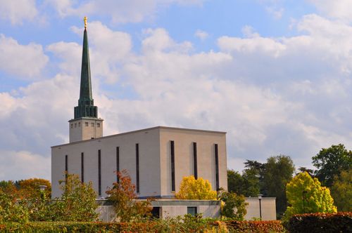 The back of the London England Temple on a fall day, showing the angel Moroni extended toward a partly cloudy sky overhead.