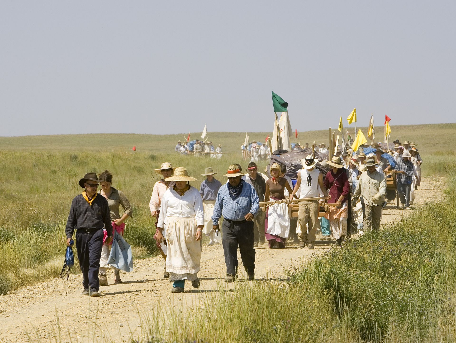 A group of men and women push handcarts down a hill amid grassy plains.