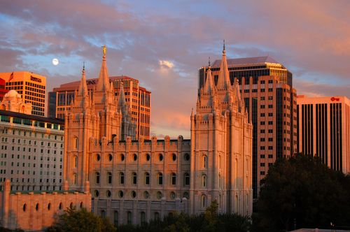 A side view of the entire Salt Lake Temple during sunset and a view of Salt Lake City in the background.