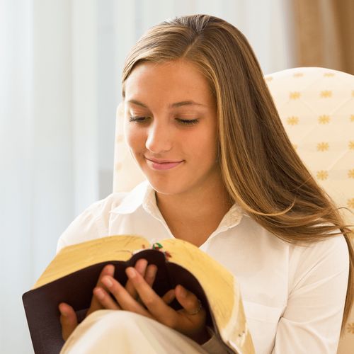 Composite of a young women sitting in an chair reading the scriptures in front of a window with curtains