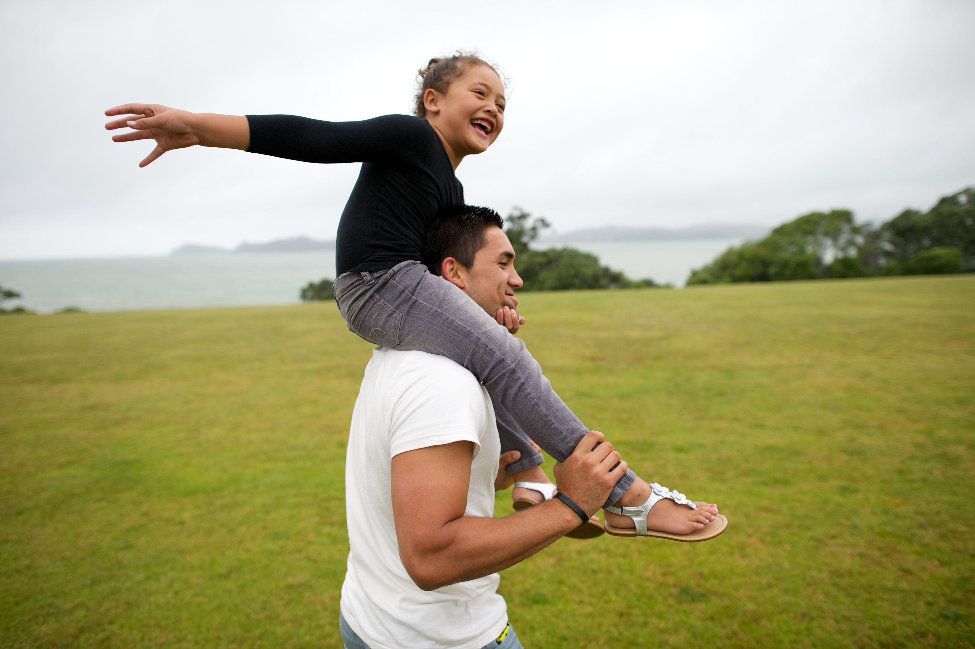 A young girl has fun with her father while she sits on his shoulders.