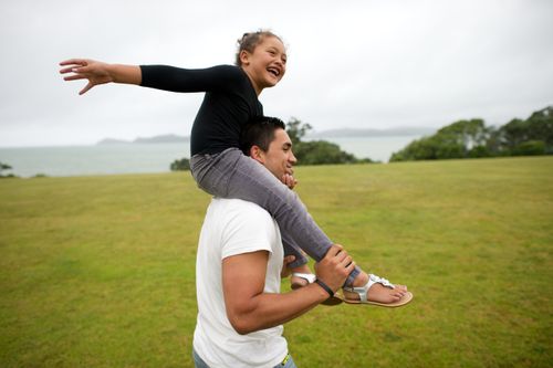 A young girl rides on her father’s shoulders while they play outside.