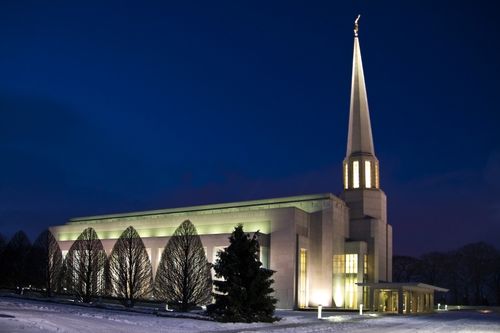 A side view of the Preston England Temple in the evening, with the temple’s lights illuminating the temple from the inside and the outside.