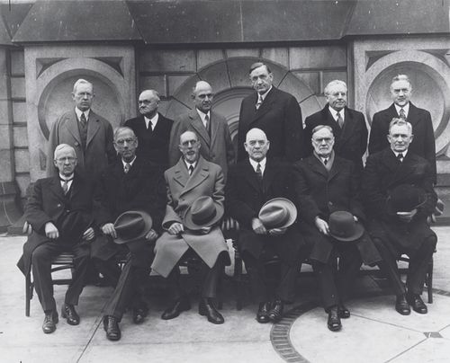 Group portrait of the Quorum of the Twelve Apostles in 1921. Included are: (left to right) seated: Rudger Clawson, Reed Smoot, George Albert Smith, George F. Richards, Orson F. Whitney, David O. McKay, standing: Joseph Fielding Smith, James E. Talmage, Stephen L. Richards, Richard R. Lyman, Melvin J. Ballard and John A. Widtsoe.