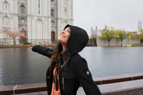 Mujer joven sonriendo bajo la lluvia delante de templo