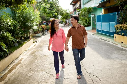 A woman with dark brown hair holding hands and walking with her husband in a brown shirt down the middle of a street in the Philippines.