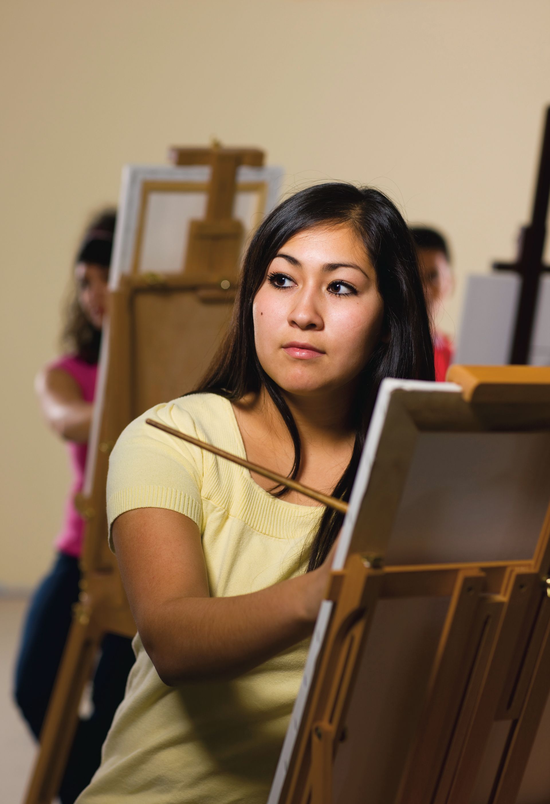 A young woman sits at an easel and paints.