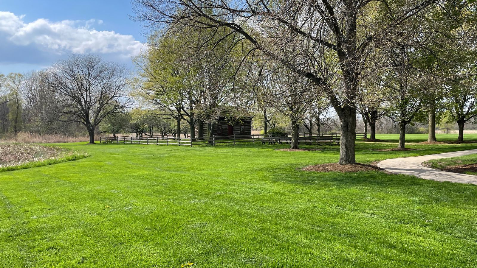 A grassy area with benches and a log home surrounded by trees in the background.