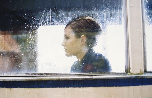 young woman looking sad through rainy window