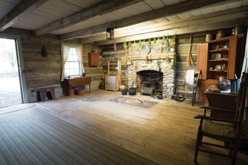 The interior of a log cabin with a stone fireplace and wooden beams holding up the ceiling.