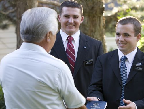 Elder missionaries giving an elderly man a Book of Mormon.