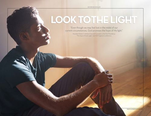 A young man sits on the floor, looking contemplatively toward a bright light.