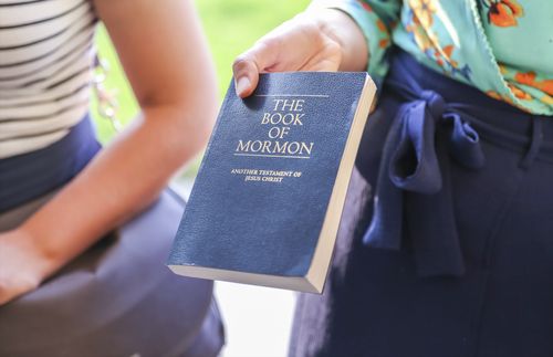 Woman holding out a Book of Mormon