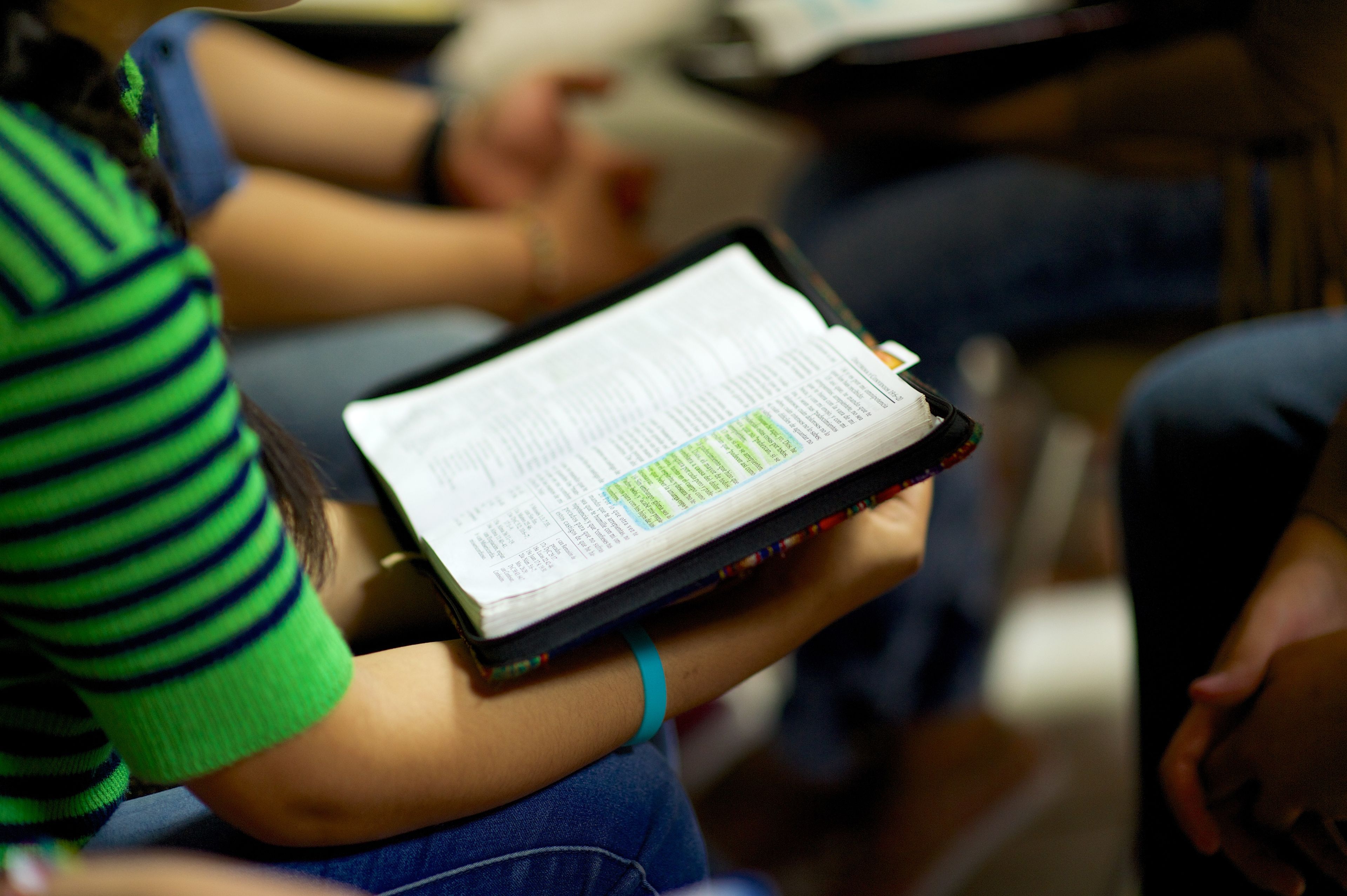 A girl holding a set of scriptures open during a group discussion.