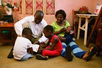 An African family seated in front of a sofa in their living room.  They are reading the scriptures.  Taken in Ghana, West Africa.