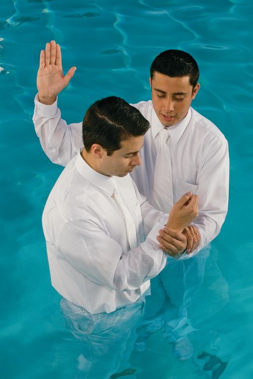 A Hispanic missionary baptizing a Hispanic man in a large font or pool.
