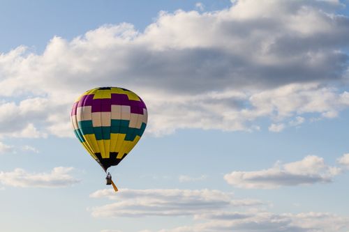 A colorful hot air balloon flies up in the blue sky, with white clouds behind it.