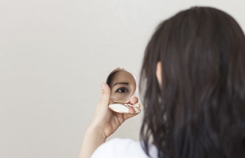 woman looking at herself in a compact hand mirror