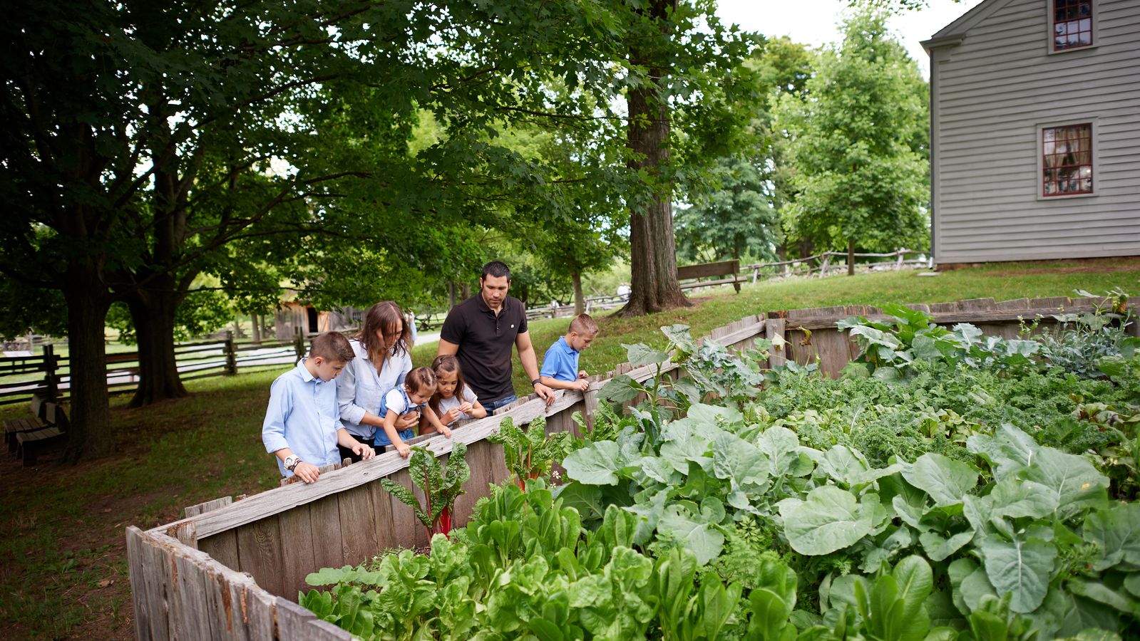 An exterior view of Joseph Smith's family garden in Palmyra, New York. 
A family walks by the garden outside the home.