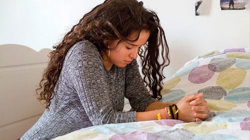 Girl kneeling at bed in prayer