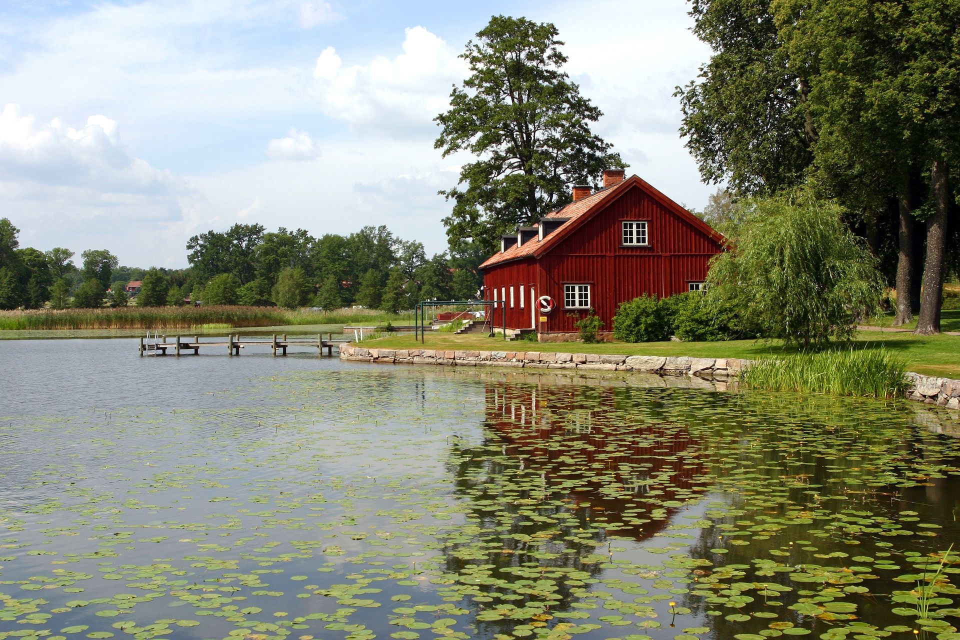 A red house in Sweden sits by a small lake filled with lily pads.