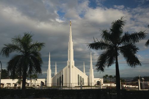 A distant view of the Manila Philippines Temple, with palm trees surrounding and storm clouds behind.