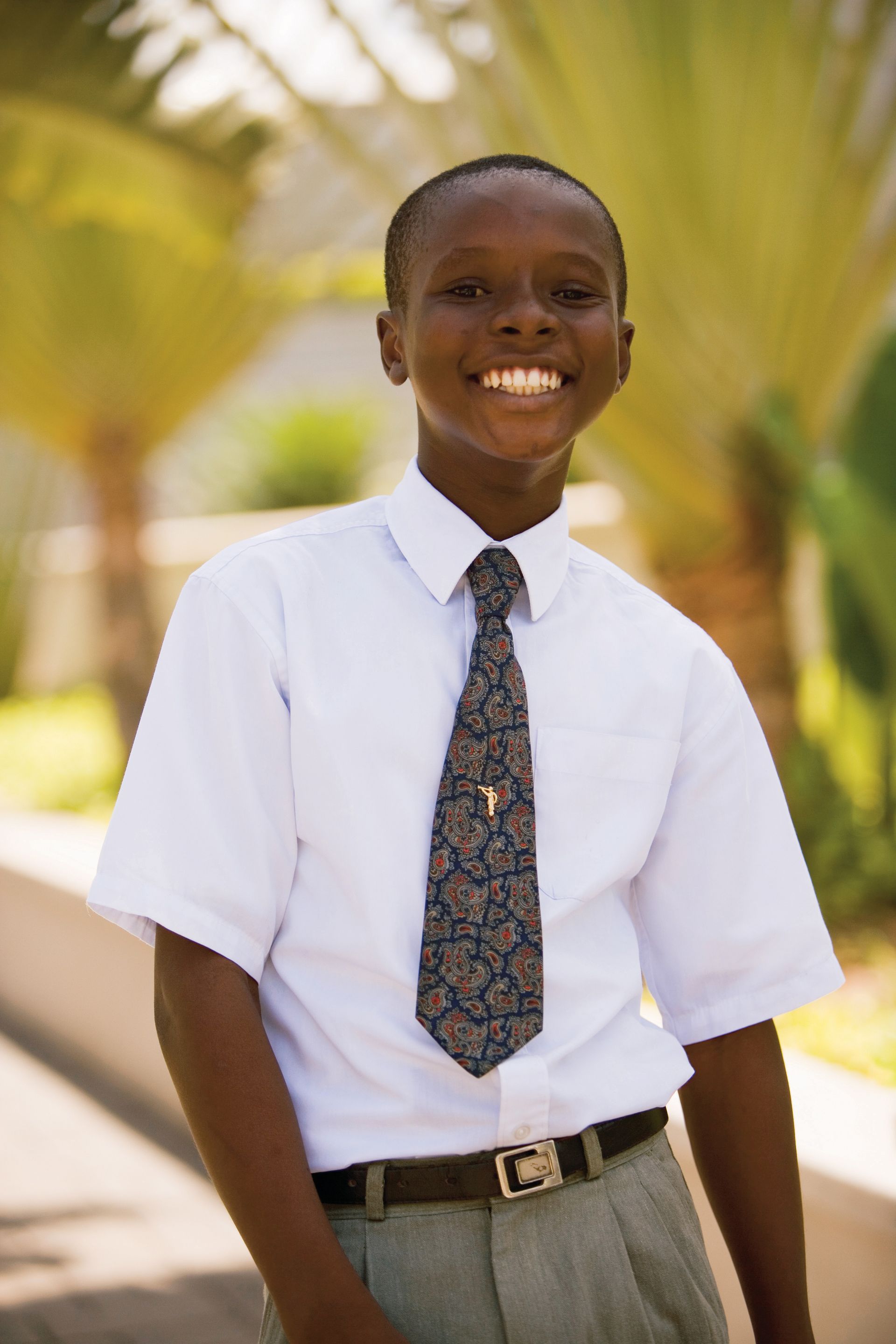 A portrait of a young man in Ghana, wearing a white shirt and tie, standing outside.