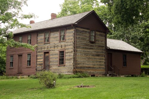 Log and clapboard building with an attached lower wing and two brick chimneys.