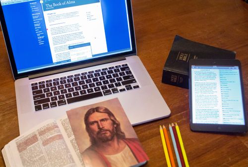 picture of Jesus Christ, physical scriptures, scriptures open on computer and tablet, and colored pencils