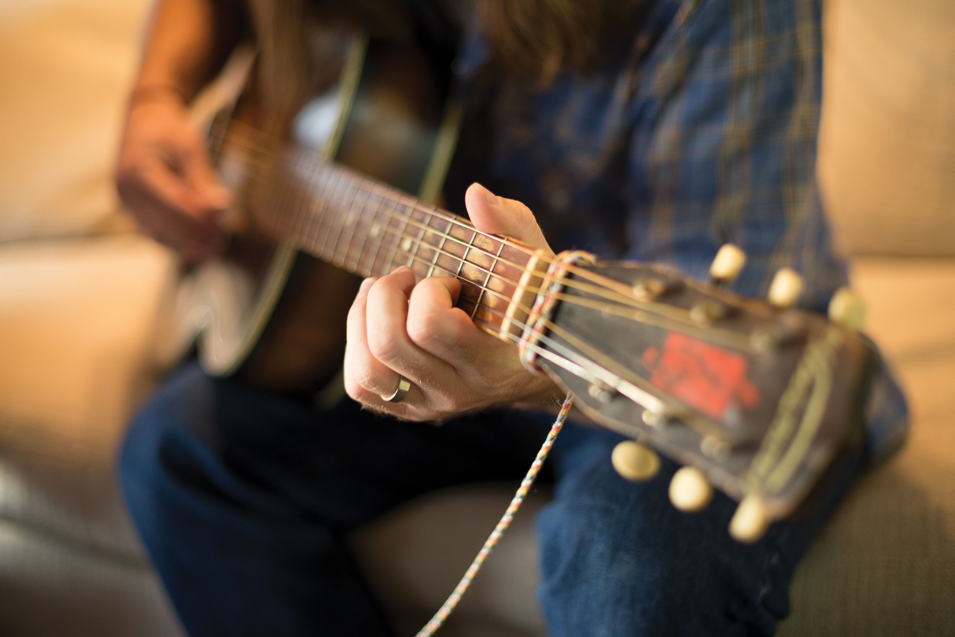 The hands of a young man are seen strumming a guitar.