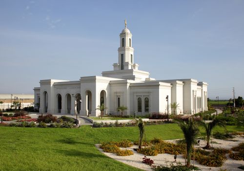 A side view of the Trujillo Peru Temple on a sunny day, with palm trees and other local plants growing on the grounds.