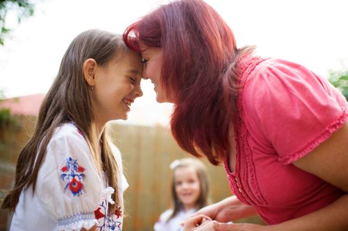 A red-haired woman presses her forehead to her daughter’s face while the two of them share a laugh together.