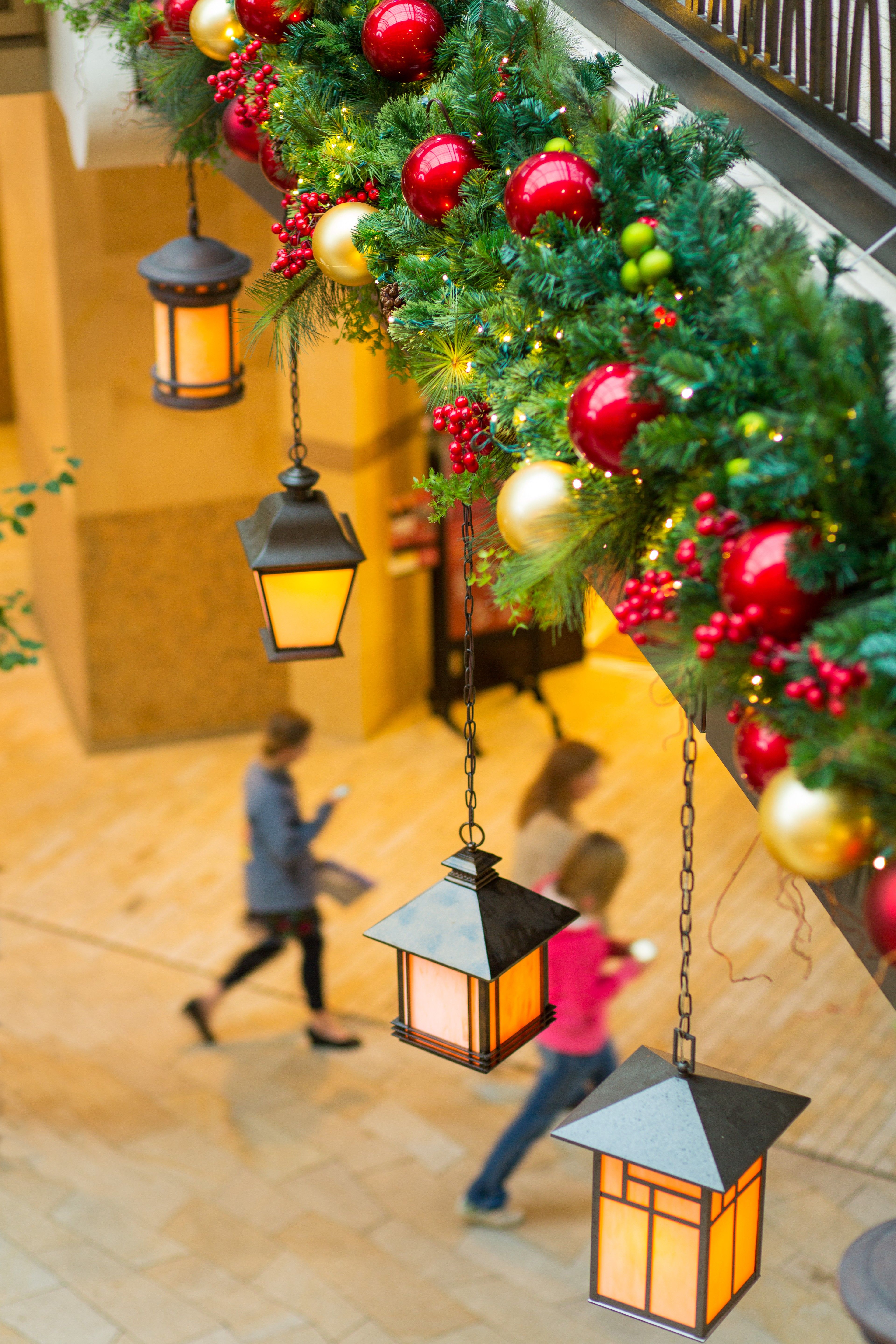 A row of lanterns and a pine bough hang over a walkway in a shopping mall.