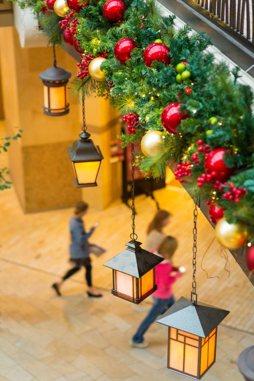A row of lit lanterns and a decorated pine bough overhanging a stone walkway in the City Creek mall.