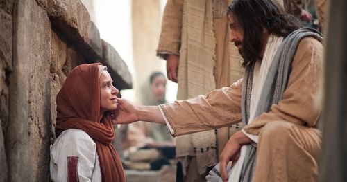 Jesus berührt die Wange einer Frau, die auf dem Boden sitzt  