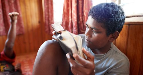 A young man is in his home. He is reading and studying scriptures. This is in Fiji.
