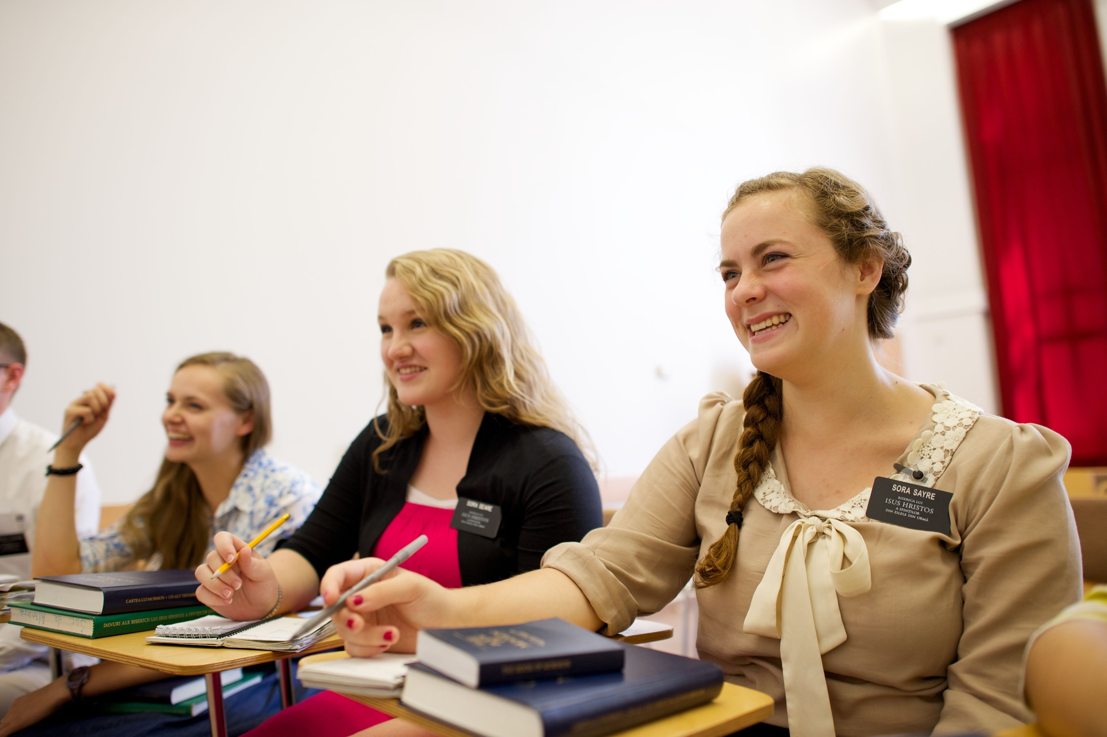 Three sister missionaries laughing while sitting at desks.