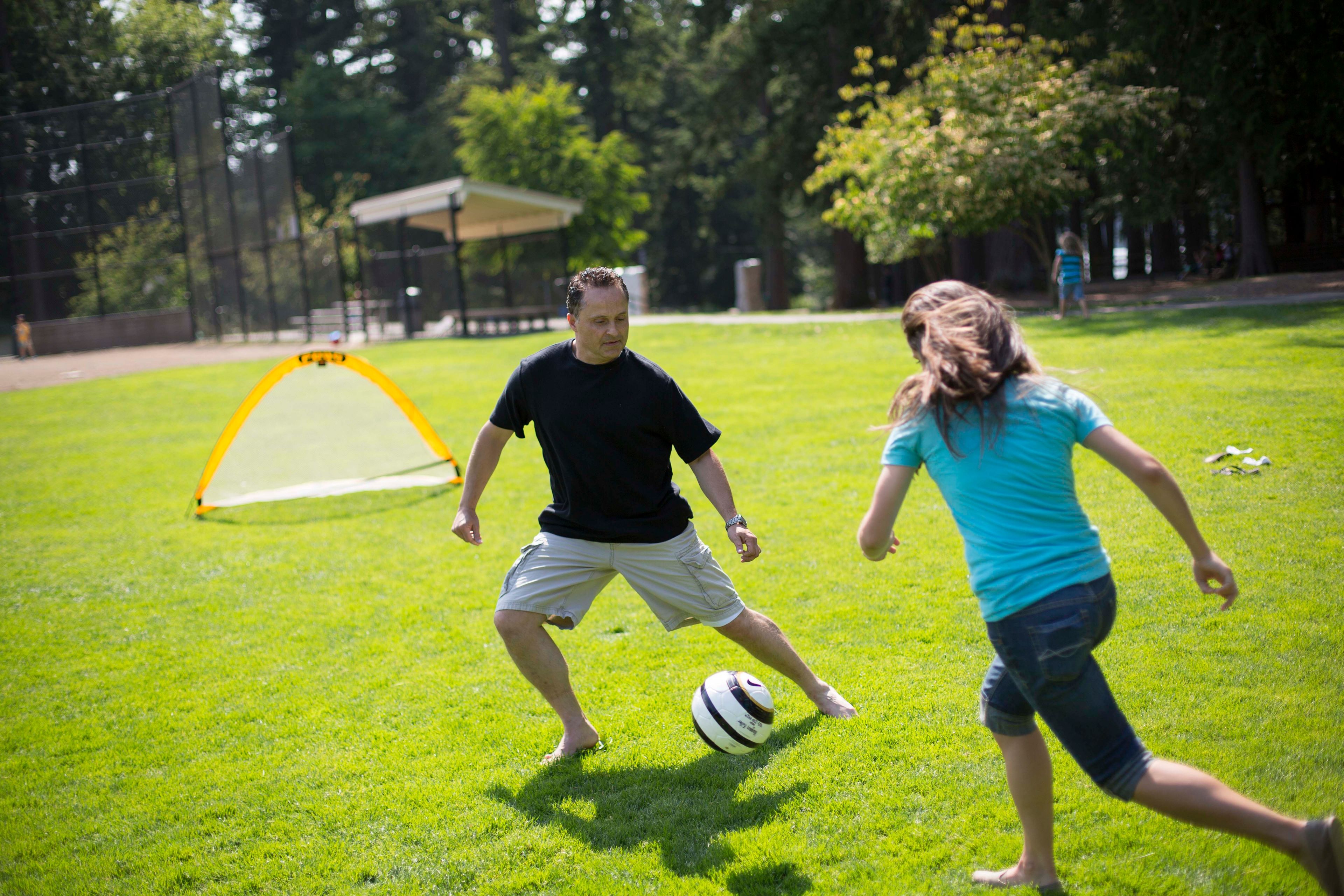 A father plays soccer with his daughter.  