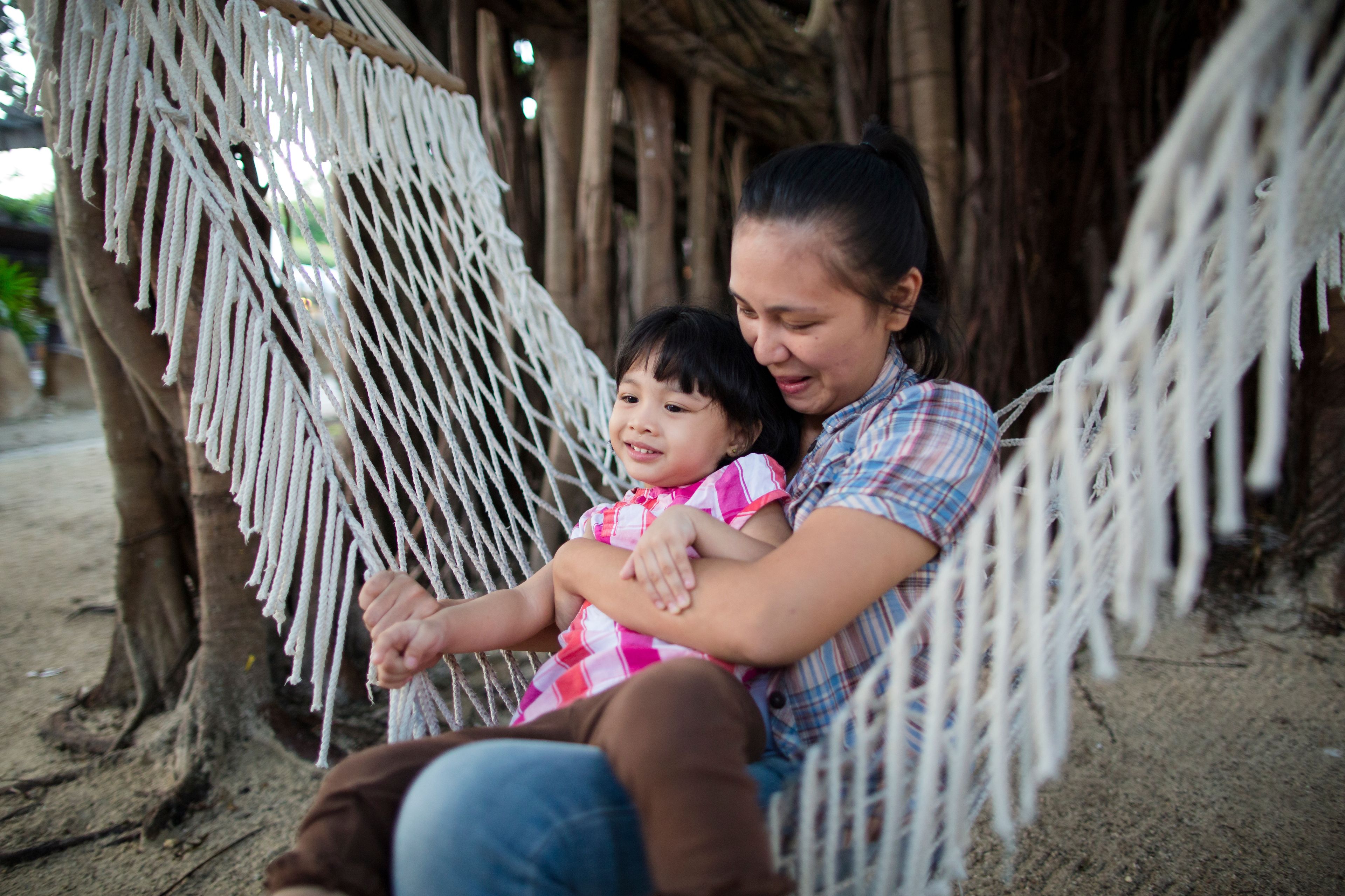 A woman holds her daughter while the two of them swing in a hammock.